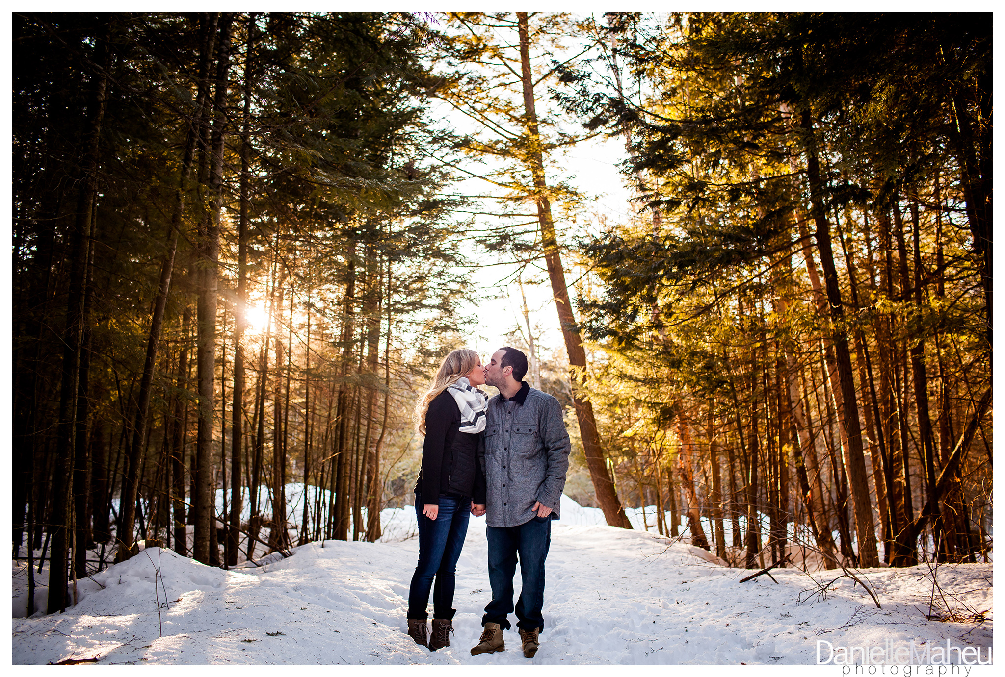Engaged couple stands in a wooded forest holding hands and kissing