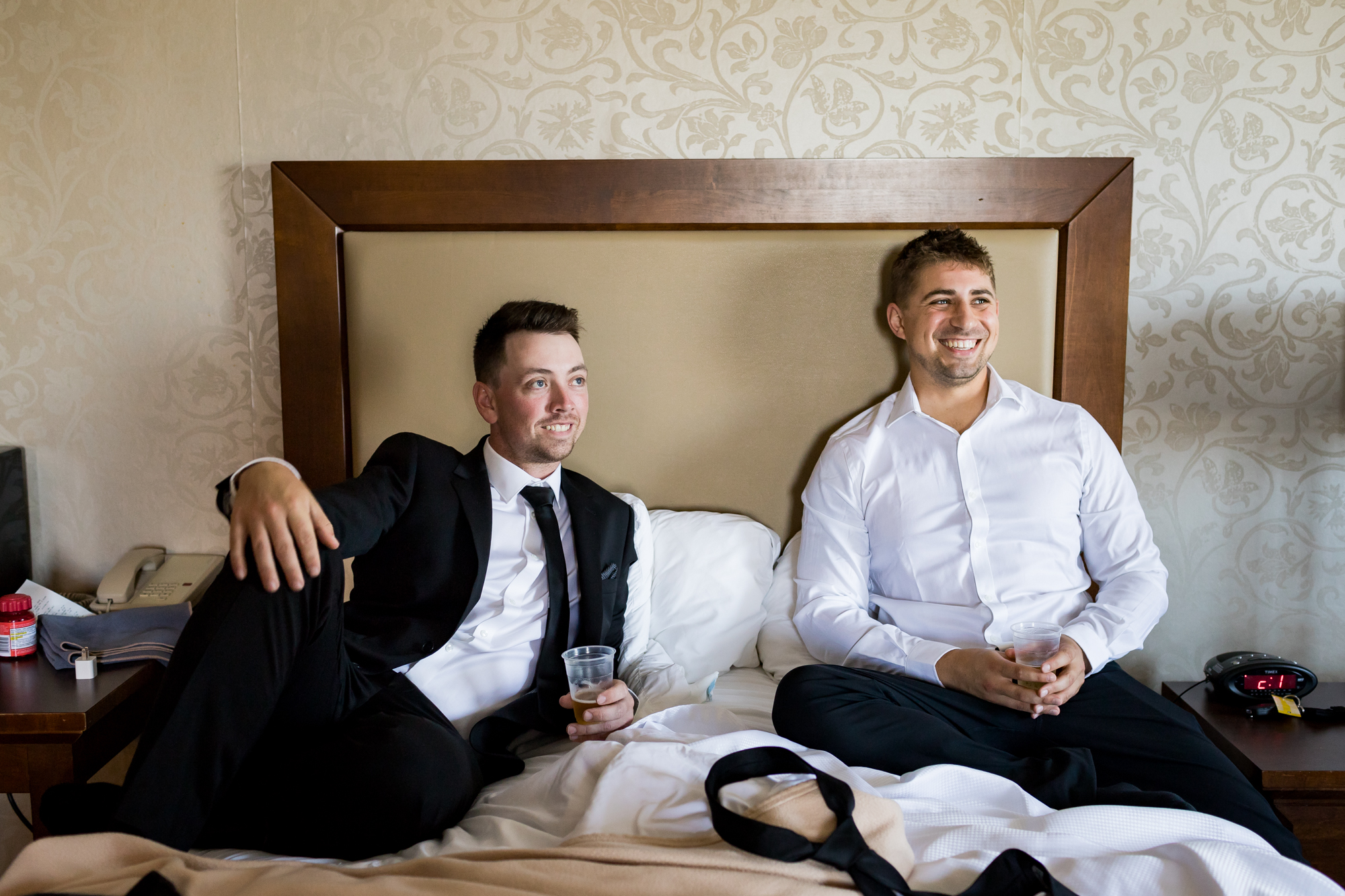 Groomsmen sitting on a hotel bed watching the groom get ready