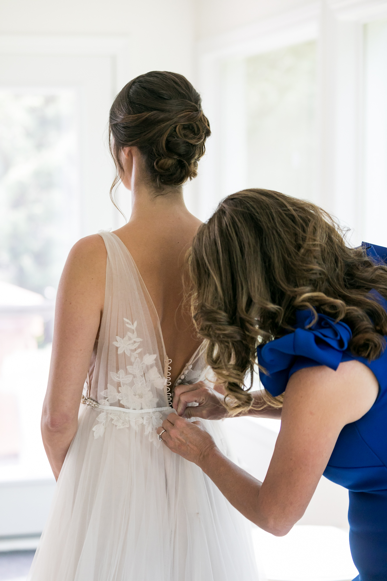 Mother of the bride helps the bride tie up her wedding dress